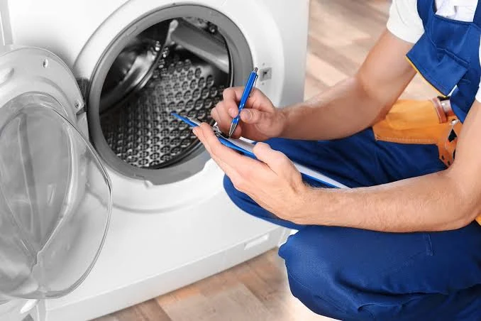 Appliance technician completing a checklist beside a front-load washing machine